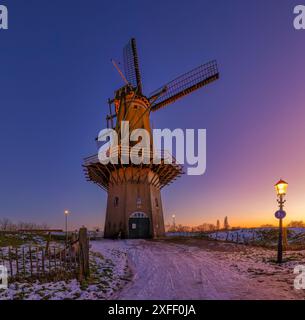 A traditional Dutch windmill in the Netherlands in winter with snow and a vibrant sunset with beautiful colors - a beautiful travel image Stock Photo