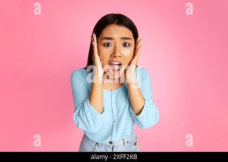 Young Woman in Blue Shirt Looks Shocked on Pink Background Stock Photo