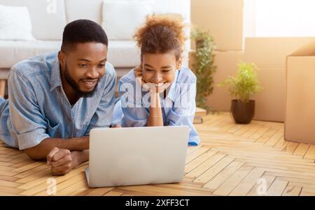 Black Spouses Using Laptop Lying On Floor Indoor Stock Photo