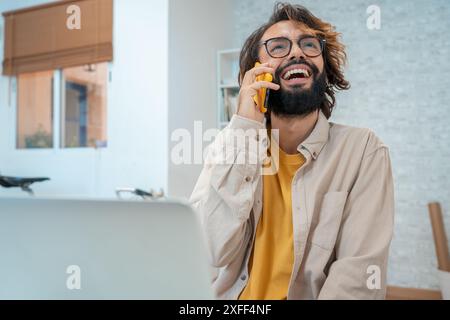 Man talking on the phone laughing in his modern workspace at home. Stock Photo