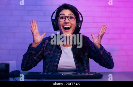 Excited Gamer Woman Wearing Headphones at Desk With Keyboard Stock Photo