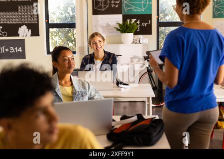 In high school, students using laptops and listening to teacher in classroom Stock Photo