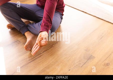 Practicing yoga, man sitting cross-legged on wooden floor, meditating at home Stock Photo