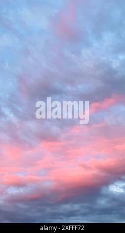 Twilight Cloudscape: Soft pink hues spread across the sky and blend with shades of blue and gray. The clouds suggest peace, serenity, and calm. Stock Photo