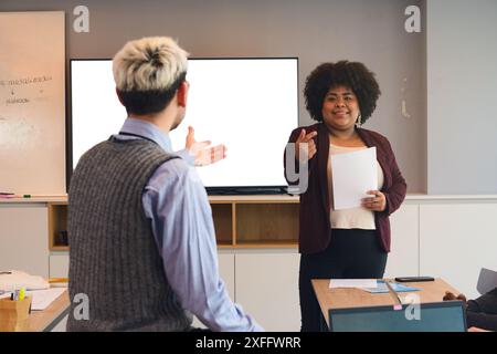 Collaborative Discussion between Man and Woman during work meeting in office, The woman has documents in her hands and is standing in front of the mon Stock Photo