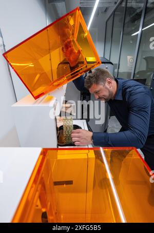 Leipzig, Germany. 03rd July, 2024. In Rapidobject's printing laboratory, Michael Walter, Production Manager, checks a component on a UV light 3D printing system. The service provider for 3D printed objects of all kinds has now opened its new glass factory. The project is designed as an open production facility. Companies and other institutions can explore the possibilities of 3D printing here. Credit: Hendrik Schmidt/dpa/Alamy Live News Stock Photo