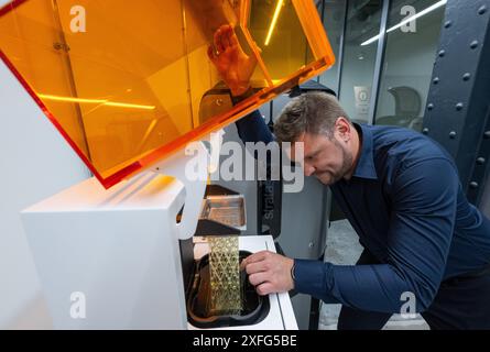 Leipzig, Germany. 03rd July, 2024. In Rapidobject's printing laboratory, Michael Walter, Production Manager, checks a component on a UV light 3D printing system. The service provider for 3D printed objects of all kinds has now opened its new glass factory. The project is designed as an open production facility. Companies and other institutions can explore the possibilities of 3D printing here. Credit: Hendrik Schmidt/dpa/Alamy Live News Stock Photo