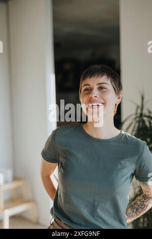 Happy woman with tattooed arm standing with hands behind back at home Stock Photo