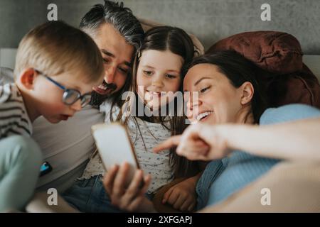 Happy family using smart phone while lying down on bed at home Stock Photo