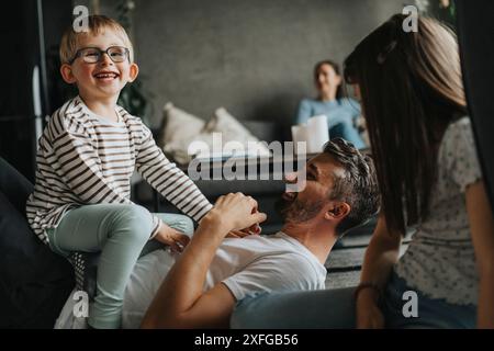 Cheerful children having fun with father lying down on floor at home Stock Photo