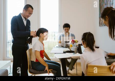 Father tying hair of daughter sitting on chair near dining table at home Stock Photo