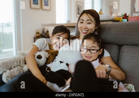 Smiling woman spending leisure time with daughters using digital tablet at home Stock Photo
