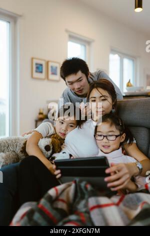 Mother and children watching digital tablet while sitting on sofa at home Stock Photo