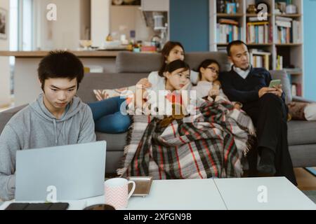 Boy using laptop with family sitting in background at home Stock Photo