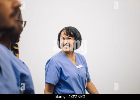 Happy senior female doctor looking at colleagues near white wall in hospital Stock Photo