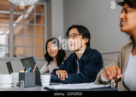 Male business professional with colleagues sitting and discussing in meeting room at office Stock Photo
