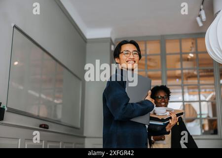 Happy male entrepreneur holding laptop while standing in meeting room Stock Photo