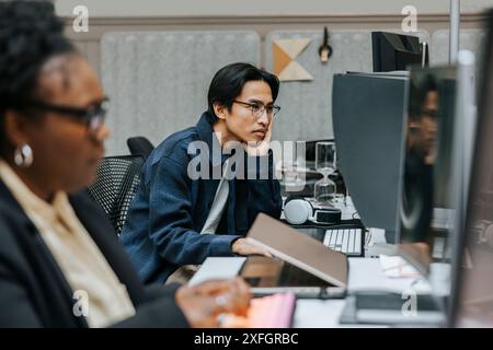 Thoughtful businessman leaning on elbow while looking at computer screen and sitting in office Stock Photo