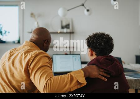 Rear view of father helping son with studies through laptop at home Stock Photo
