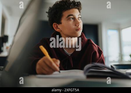 Thoughtful boy doing homework while looking away at home Stock Photo