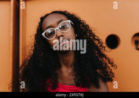 Portrait of teenage girl with curly hair wearing eyeglasses against metal structure Stock Photo