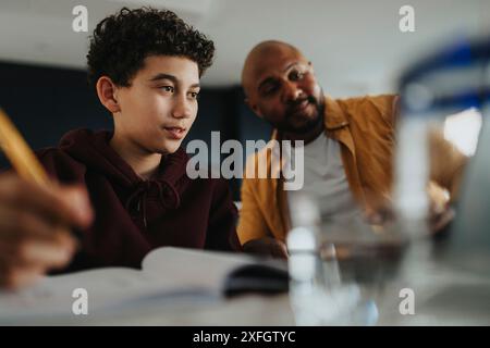 Happy father assisting son in doing homework at home Stock Photo