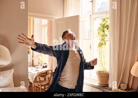 Cheerful man with arm outstretched dancing in bedroom at home Stock Photo