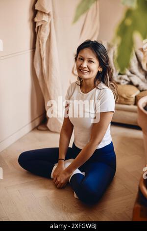 Portrait of smiling woman sitting on hardwood floor at home Stock Photo