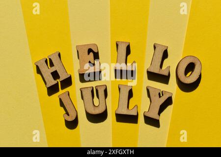 Hello July, words in wooden alphabet letters isolated on yellow background Stock Photo