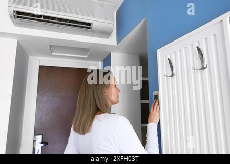 Woman controls an air conditioner from a remote control on the wall. Stock Photo