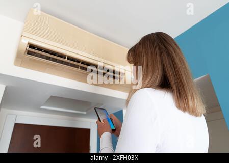 Woman controls a smart air conditioner using a remote control on her phone. Stock Photo