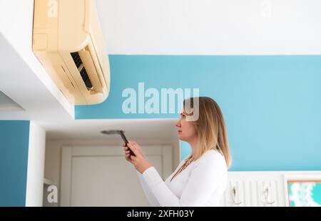 Woman controls a smart air conditioner using a remote control on her phone. Stock Photo