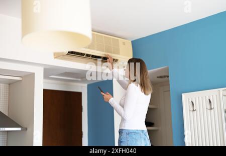 Woman controls a smart air conditioner using a remote control on her phone. Stock Photo