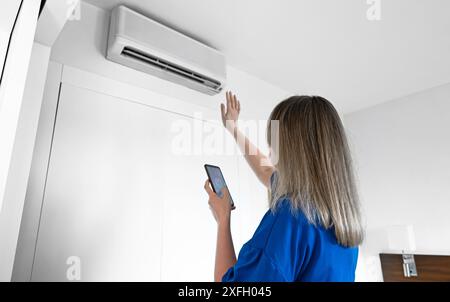 Woman controls a smart air conditioner using a remote control on her phone. Stock Photo