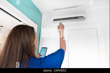 Woman controls a smart air conditioner using a remote control on her phone. Stock Photo