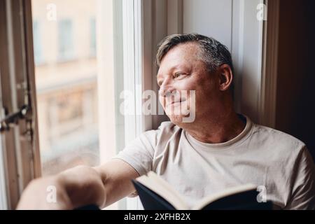 Thoughtful mature man looking through window at home Stock Photo