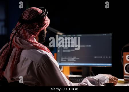 Arab software developer typing code and focused on running algorithms, showcasing his programming skills. Computer screen displays a user interface, highlighting the importance of internet security. Stock Photo