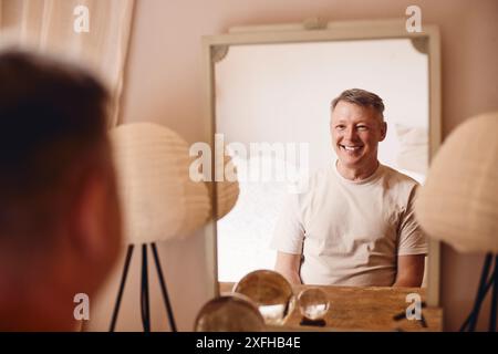 Smiling mature man sitting in front of mirror at home Stock Photo