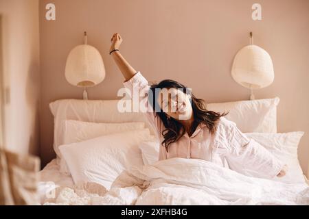 Young woman waking up from sleep while sitting on bed at home Stock Photo
