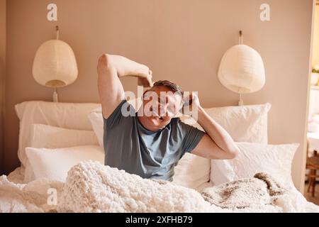 Happy mature man stretching while sitting on bed at home Stock Photo