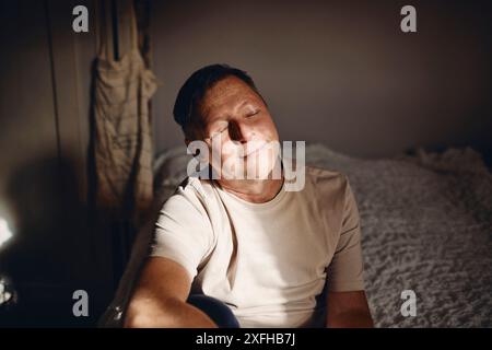 Smiling mature man sitting on bed at home Stock Photo