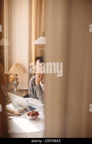 Young woman with hand on chin sitting at table in home Stock Photo