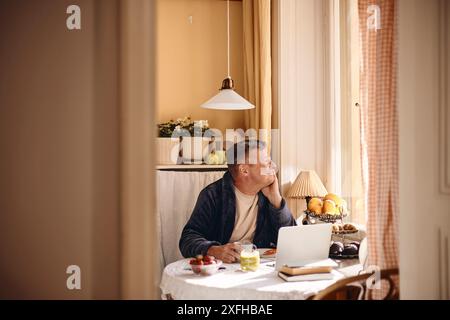 Thoughtful mature man looking through window while sitting at dining table Stock Photo