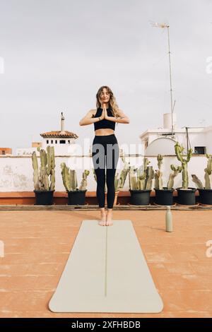 Young woman practicing prayer pose while standing on yoga mat Stock Photo