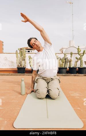 Man with eyes closed stretching arm while doing yoga on rooftop Stock Photo