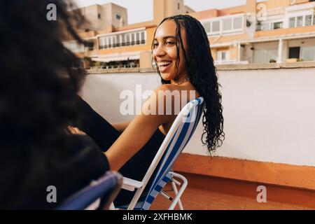Smiling woman with long hair sitting next to male friend on building rooftop Stock Photo