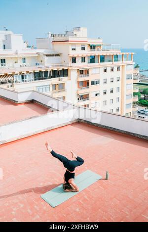 High angle view of young woman practicing headstand on building terrace Stock Photo