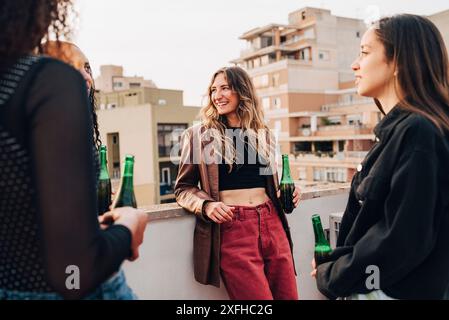 Smiling young woman spending leisure time with female friends having beer at rooftop party Stock Photo