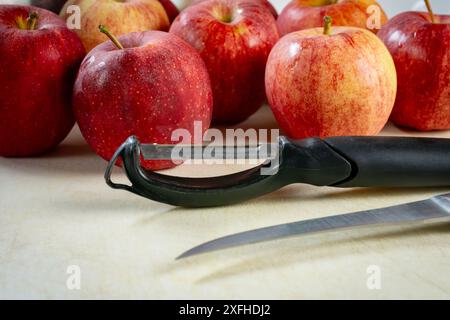 A knife and peeler on a white cutting board surrounded by gala apples.  Preparation for a pie.. Stock Photo