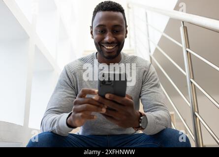 Smiling man using smartphone while sitting on stairs at home Stock Photo